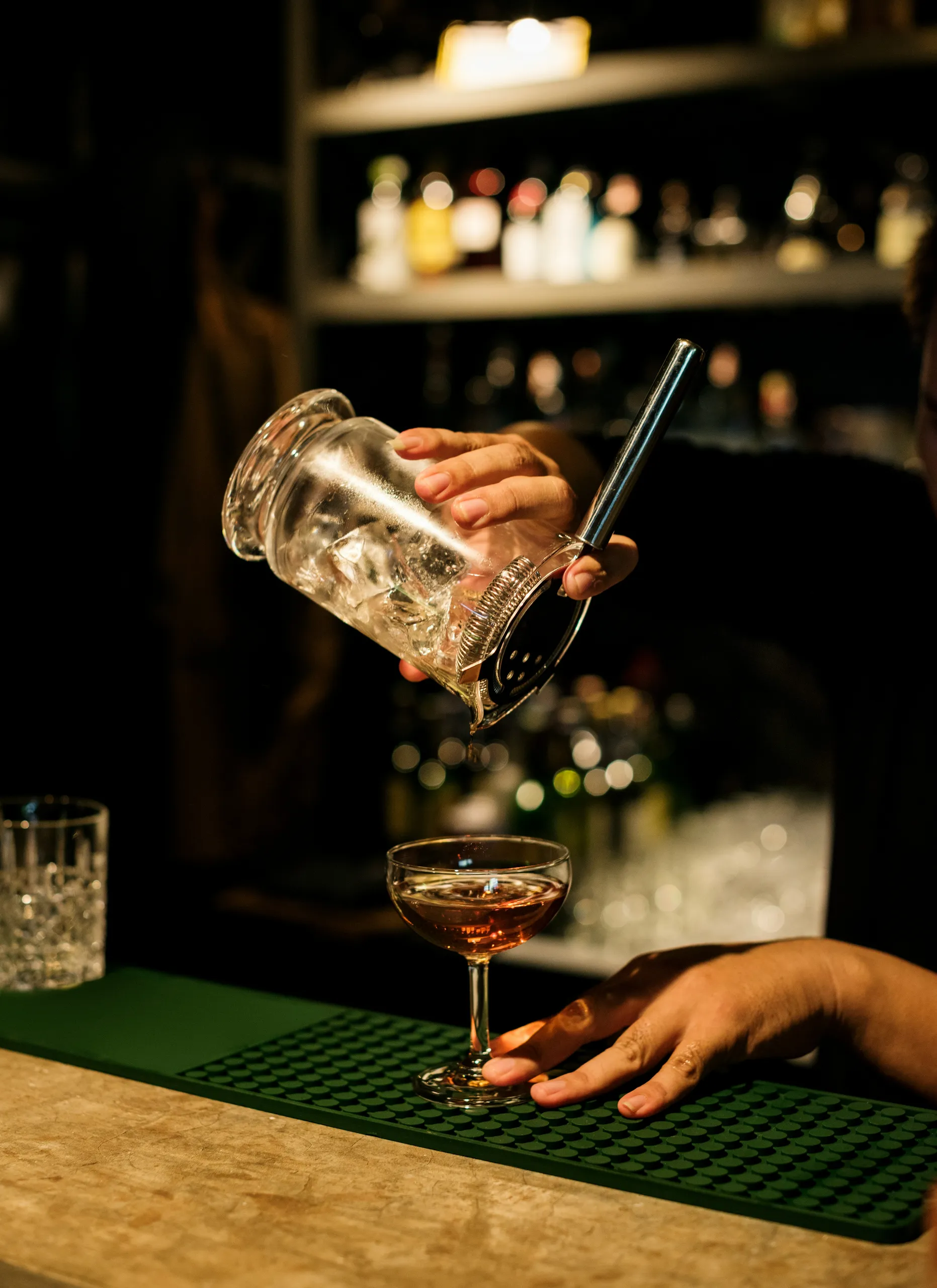 Barman przelewa koktajl do kieliszka przy ciemnym, klimatycznym barze.